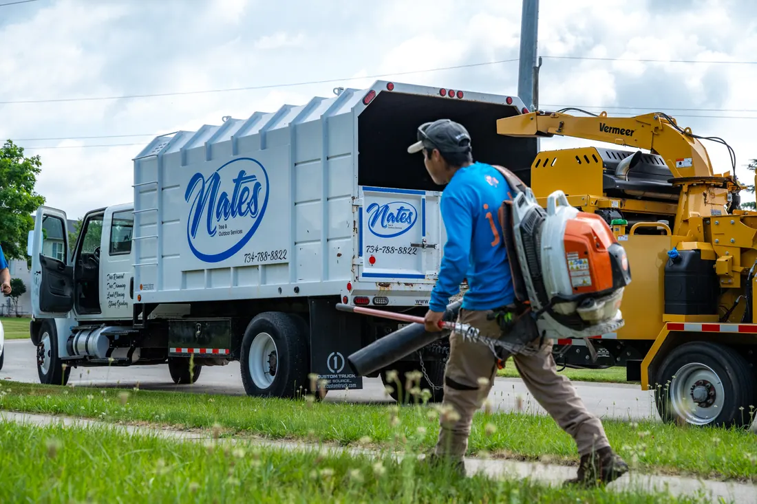 Nate's crew member clearing yard debris with a backpack blower beside the chipper and truck
